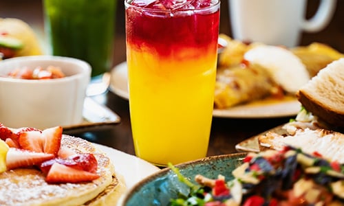 Table full of brunch items, including: Lemon Ricotta Pancakes with fresh strawberries, and Kale Tonic fresh juice