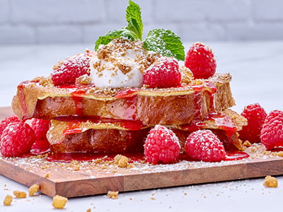 Thick-cut, custard-dipped challah bread griddled and topped with fresh raspberries, whipped lemon ricotta cream, raspberry purée and spiced gingerbread cookie crumbles. Lightly dusted with powdered cinnamon sugar and garnished with mint.