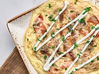 A classic frittata with Wild Alaska Smoked Sockeye Salmon, house-roasted shallots and tomatoes topped with Parmesan, a chive cream drizzle and fresh herbs. Served with ciabatta toast and lemon-dressed organic mixed greens.